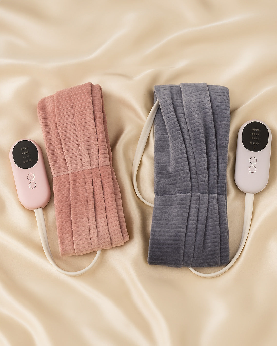 Two hair heating pads, one pink and one gray, with controllers on a beige fabric background.