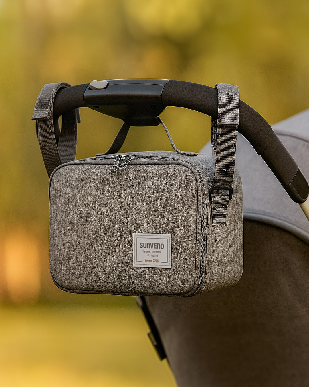 Grey baby diaper bag attached to a stroller with a blurred natural background