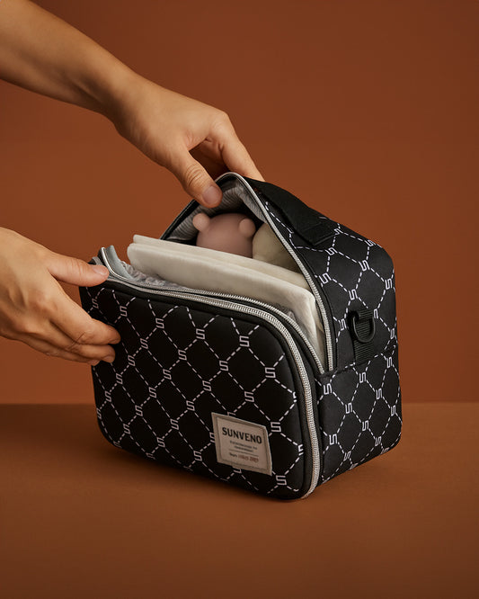 Black quilted baby diaper bag with white geometric pattern held by hands on a brown background