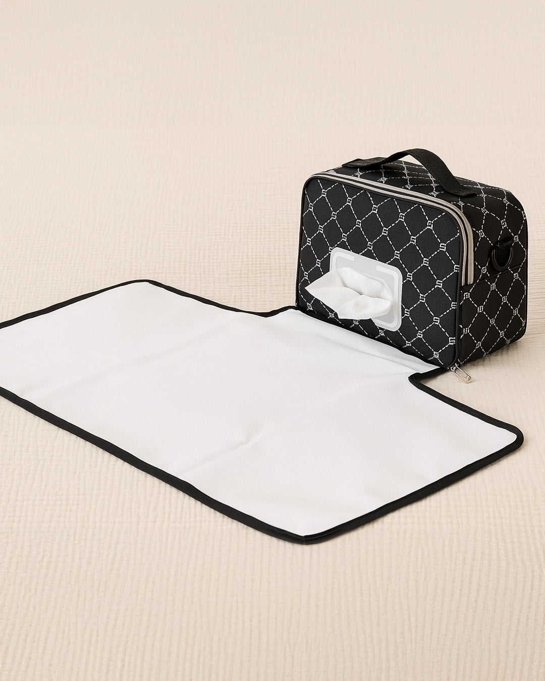 Black quilted diaper bag with a white changing mat on a beige surface