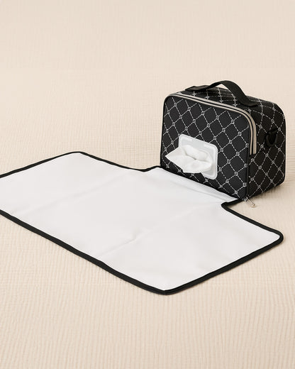 Black quilted diaper bag with a white changing mat on a beige surface