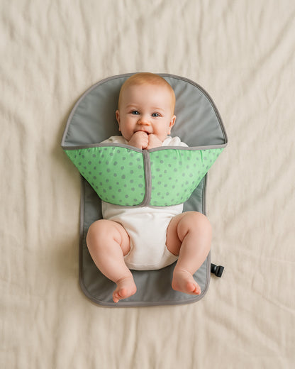 Baby sitting in a green and grey baby change pad on a beige blanket