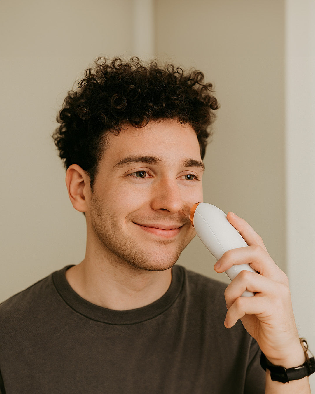 Man using a white acne device on his face against a neutral background