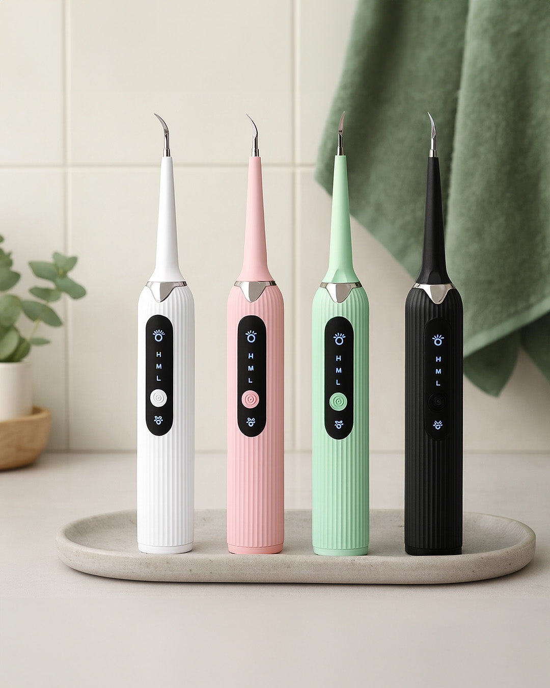 Four electric toothbrushes in white, pink, green, and black on a tray with a green towel in the background.